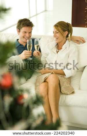 Couple sitting on couch, making a toast with champagne, smiling