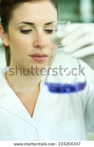 Female lab worker holding up flask, inspecting its contents