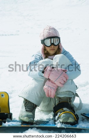 Young female snowboarder sitting on ground, hugging knees