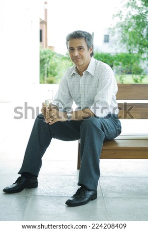 Man sitting on patio holding glass of champagne, full length