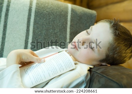 Boy reclining on couch, holding book, eyes closed
