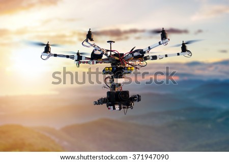 The drone with the professional cinema camera flying over the misty mountains at sunset. Blurred background.