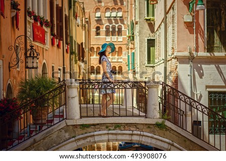 Travel to Italy. Young woman in summer dress and blue hat with camera posing on the bridge in Venice. Venice is popular tourist place in Europe.