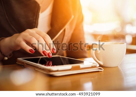 Tablet PC close up photo with woman hands macro shot. Girl using tablet in the cafe and drinking tea. Blurred background with lens flare effects.