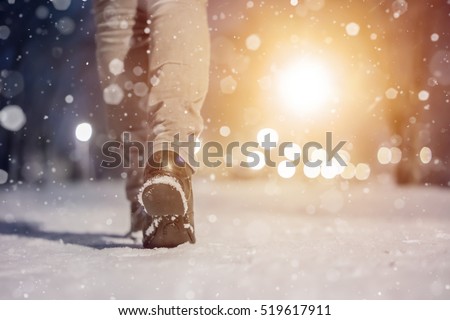 macro photo of  woman boots. Girl walking in winter city park evening. Closeup of winter shoes. Blurred lens flare background with copy space area for a text. Snowfall in the winter park.