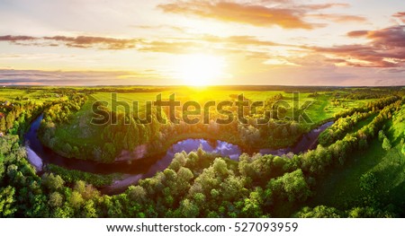 Majestic sunset in the nature landscape. Aerial panorama of blue calm river in the forest and fields at the sunset. Summer nature landscape. Dramatic cloudy sky. View of nature forest landscape