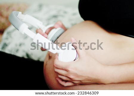 Pregnant woman with headphones on the bed and listening to music in the bedroom