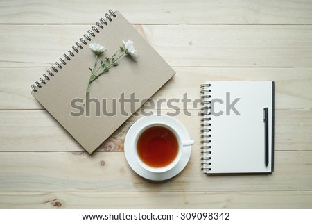 opened notebook with cup of tea and tiny flowers on wooden table. Top view. Writing concept