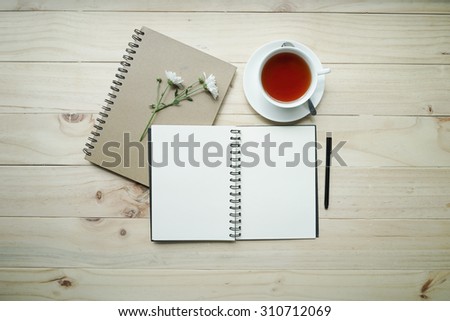 blank opened notebook with cup of tea and flowers on wooden table. Top view. Writing concept