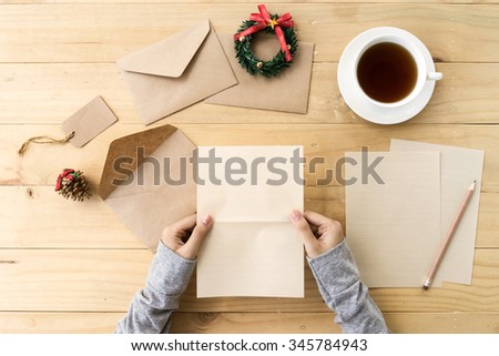 Letter for Santa. Female hand holding blank letter paper on wooden table  with cup of tea and Christmas decorations