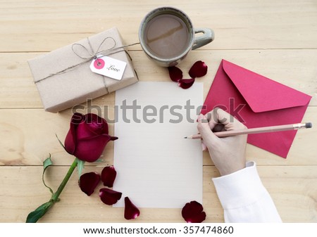 Female hands writing down on letter paper for Valentine\'s day with gift box and cup of coffee on desk, top view