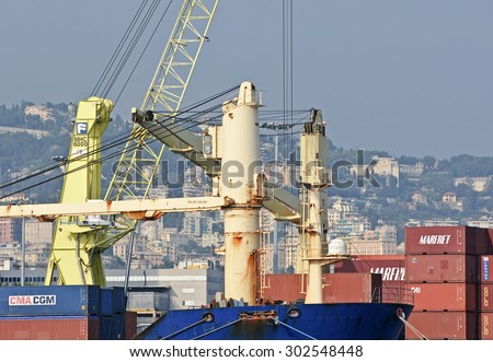 GENOA, ITALY - JULY 21, 2015: Towering crane on the deck of the cargo ship. On the docks the containers of CMA CGM and MARFRET respectively shipping companies.