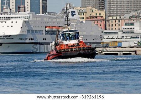 GENOA, ITALY - MAY 20, 2014: Tugboat at work in the waters of the ferry terminal. In the background the quay, the city and the ferry.