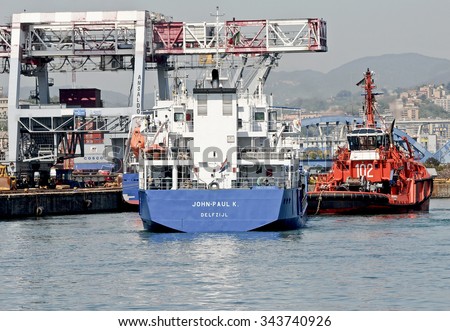 GENOA, ITALY - APRIL 27, 2012: The tug Messico and general cargo Jhon Paul under way in the Genoa port. In the background, the quay with cranes of the ILVA plant.