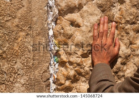Hand man praying at the Wailing Wall with notes in the wall with requests