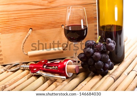 Wine glass with red wine, bottle opener, grapes, box wine and a bottle on bamboo