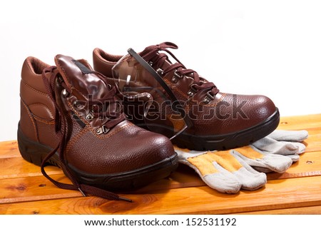 Working brown shoes with laces, gloves and safety glasses on a wooden bench