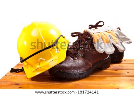 Working boots and gloves, yellow hard hat with goggles on a wooden bench