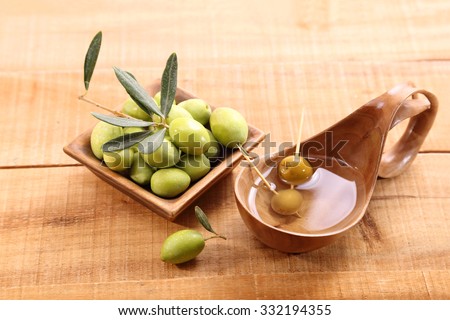 Green olives and oil in a ladle made of olive wood on the table
