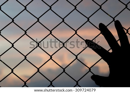 hand put on the metallic fence at the sunset