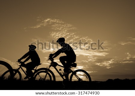 Blurred silhouette of people Image of sporty company friends on bicycles outdoors against sunset, motion blurred