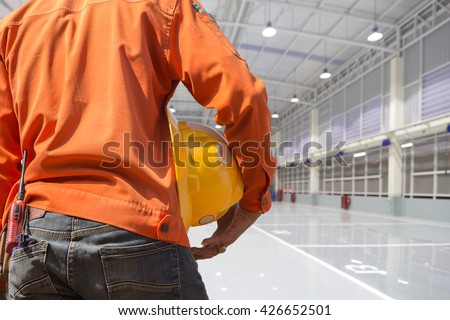 engineer holding yellow helmet for workers security on indoor factory epoxy floor construction site background