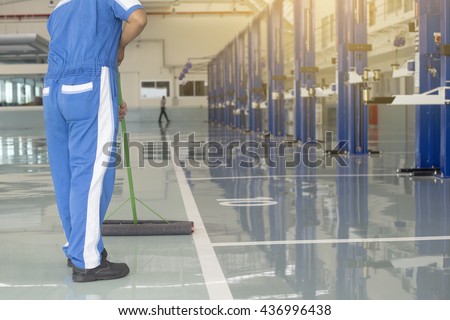 worker in blue, protective uniform cleaning new epoxy floor in empty storehouse or car service center