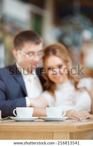 Two cups of coffee or tea, stand on a table in a restaurant on a background of a loving couple, man and woman bride groom.