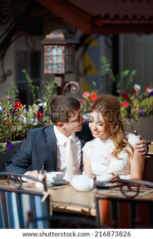 Two beautiful young people, bride and groom sitting at a table in a cafe.With a good mood, they are celebrating their wedding day, drinking coffee from a white cup.