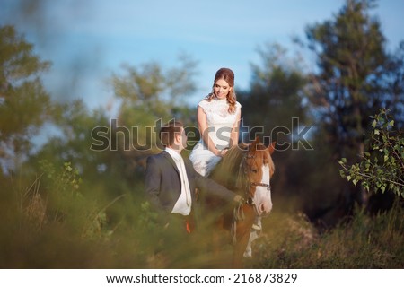 Bride and groom, wedding love story. Happy newlyweds embracing each other, walk in the park in the open air, Horseback riding. Newly married man, woman sitting in the sun, walking around their horse.