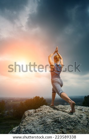 Woman doing yoga against the setting sun. Fitness classes outdoors. Stormy sky with sunshine. Attractive fitness woman, lifestyle portrait, caucasian model