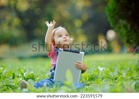 Child playing with tablet outdoors. Cheerful child with a portable PC in your hands. The kid looks away.