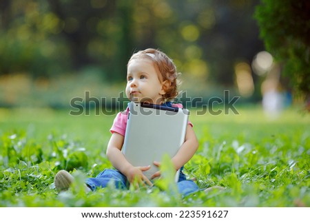 Child playing with tablet outdoors. Cheerful child with a portable PC in your hands. The kid looks away.
