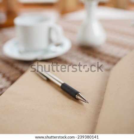 Pen and notebook on the table in a cafe, standing next to a cup of tea, teapot and vase with a bouquet of flowers