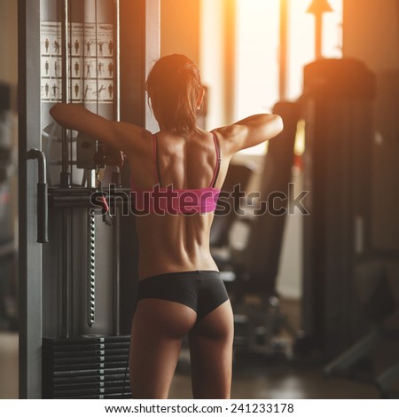 Athletic young woman showing muscles of the back and hand. Athletic young woman doing a fitness workout