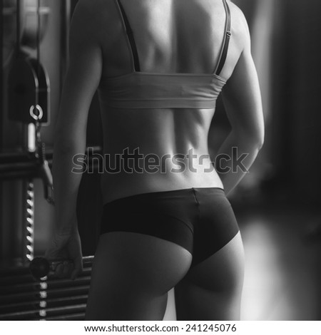 Black and white photo of a strong woman. Brunette sexy fitness girl in sport wear with perfect body in the gym posing before training set