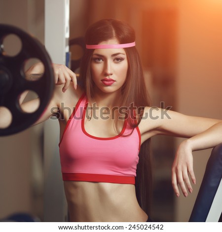 Sexy brunette with long hair and sporting appearance posing in the gym. Young fitness woman in pink t-shirt trainers at the gym.