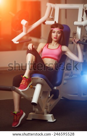 Sexy brunette with very long hair and sporting appearance posing in the gym under the rays of blue and orange light. Young fitness woman in pink t-shirt trainers at the gym.