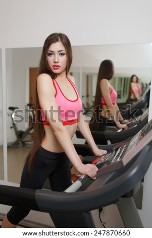 Sexual long-haired brunette, athletic appearance, is engaged on the treadmill at the gym