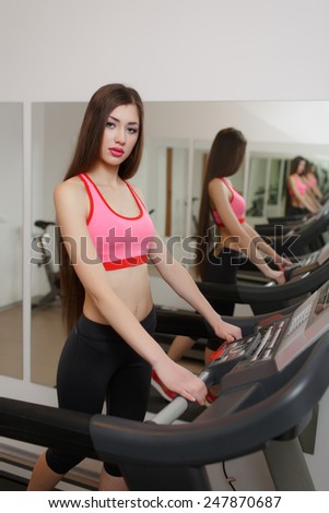 Sexual long-haired brunette, athletic appearance, is engaged on the treadmill at the gym