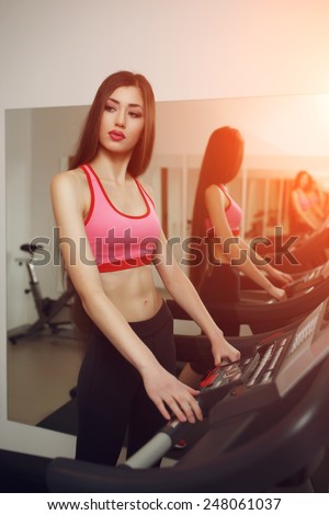 Sexual long-haired brunette, athletic appearance, is engaged on the treadmill at the gym. Instagram toning effect.