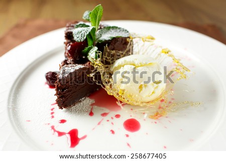 Chocolate brownie with cherries and vanilla ice cream garnished with powdered sugar and mint leaf on a white plate