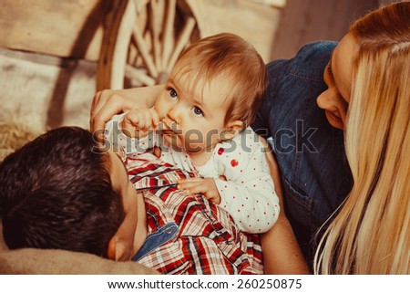 Happy village family, mom and dad playing with a small child lying on the hay