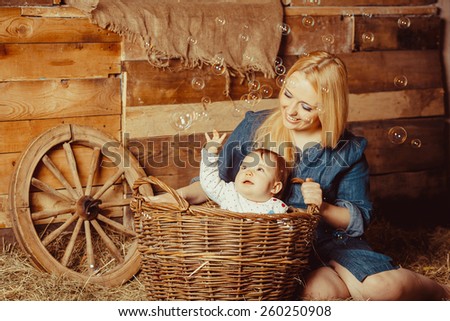 Happy village family, mom playing with a baby in a basket sitting on the hay. Little girl sitting in a basket with hay