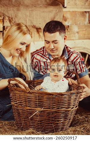 Happy village family, mom and dad playing with a small child sitting on the hay