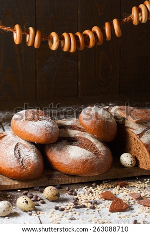 Variety of rye bread on a wooden background with milk, a bundle of bagels, flour, grain and quail eggs