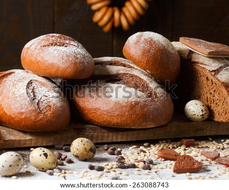 Variety of rye bread on a wooden background with milk, a bundle of bagels, flour, grain and quail eggs