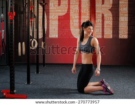 Workout on rings. Fit woman training session on the rings in the gym. Attractive muscular woman, caucasian appearance, brunette is kneeling in the gym and looking to the side
