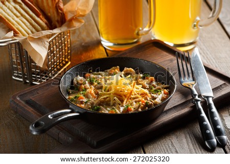 Roast with mushrooms, garlic sauce and chopped greens served in a frying pan on a wooden board, standing next to a glass of beer and golden pieces of bread