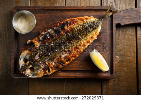 One baked mackerel, served on a wooden board with lemon sauce